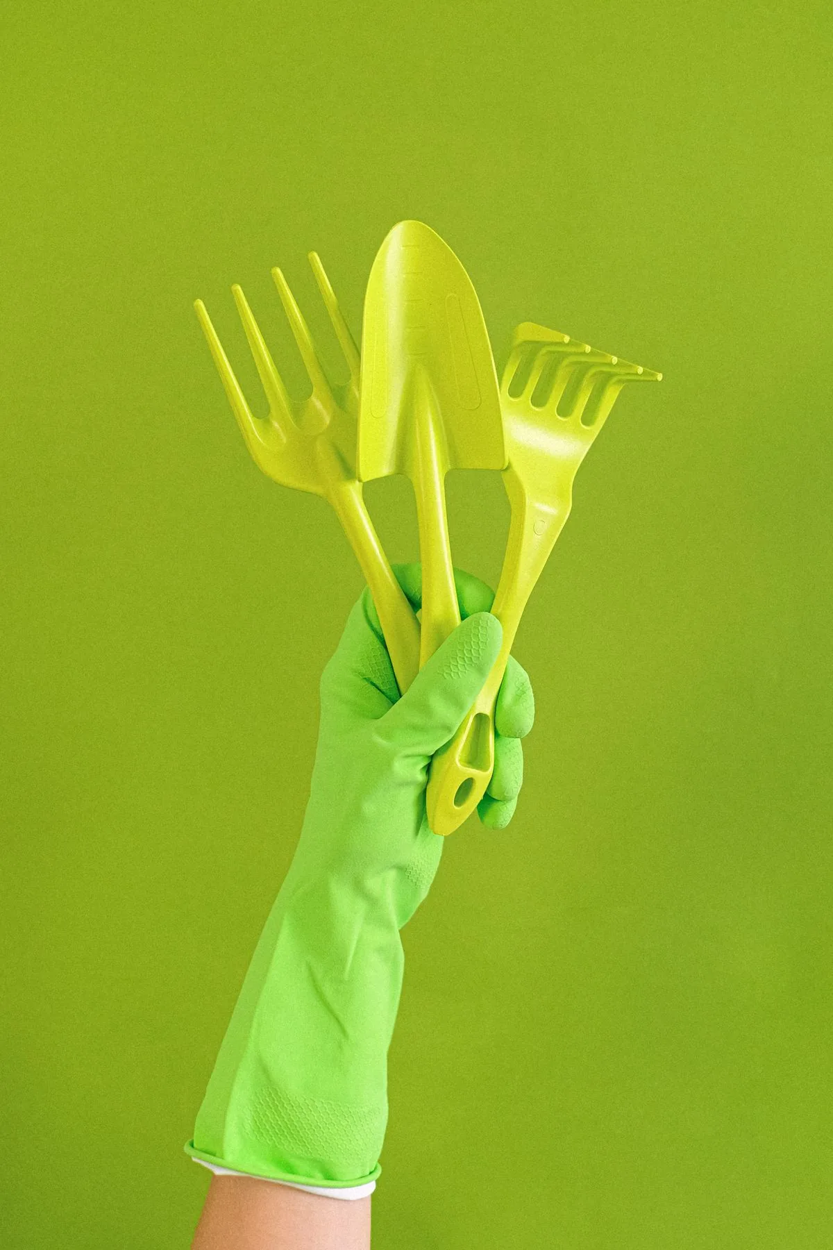 Mano con guante de goma sosteniendo herramientas de jardín